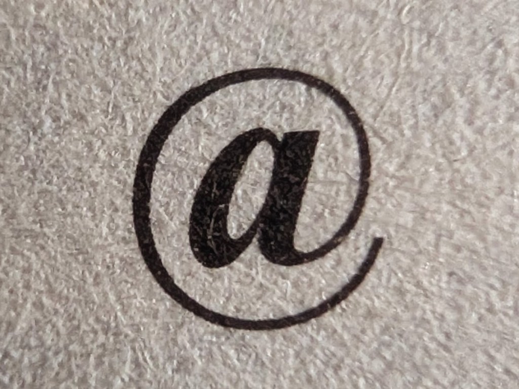 Photograph of an '@' symbol printed in black ink on white paper.