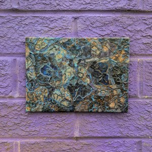 Photograph of a small, landscape-orientation mixed media artwork featuring organic mark-making in a colour palette of blues, greys and yellows.

The artwork is set against a brick wall covered in purple spray paint.