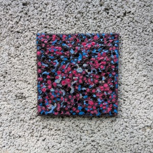 Photograph of a small, square mixed media artwork featuring organic mark-making in a colour palette of blues, browns and pinks. The artwork is set against grey breezeblock.