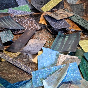 Photograph of a messy heap of mixed media work on paper of different kinds, featuring organic mark-making in a colour palette of browns, greens and blues.